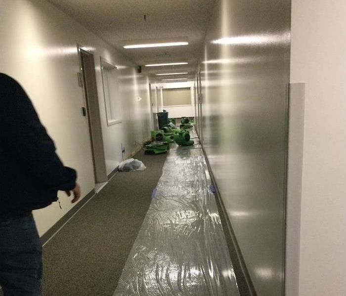 Commercial office hallway with dehumidifiers and containment material during the mitigation process